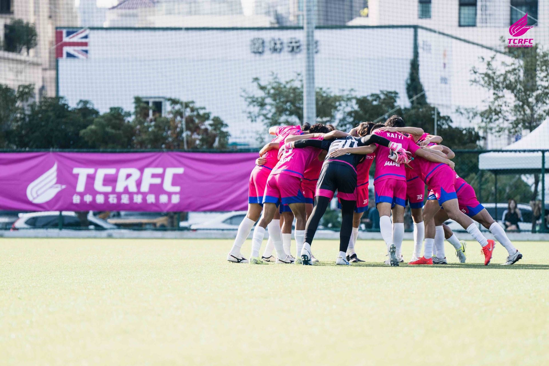 台中磐石足球俱樂部一線隊球員賽前於場邊圍圈激勵士氣，場邊懸掛桃紅色 TCRFC 布條